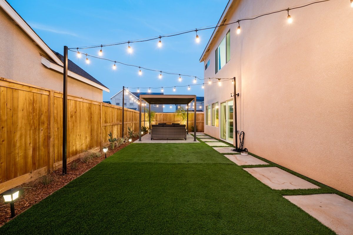 Backyard lawn with string lights and a covered seating area at dusk